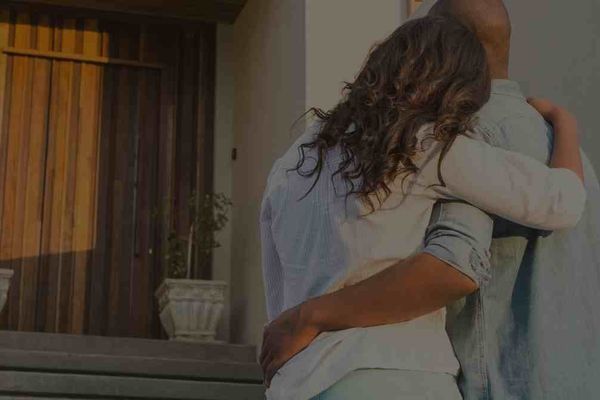 Happy Scottsdale home buyers in front of the wooden front door of their new place with a SOLD sign in front of it.